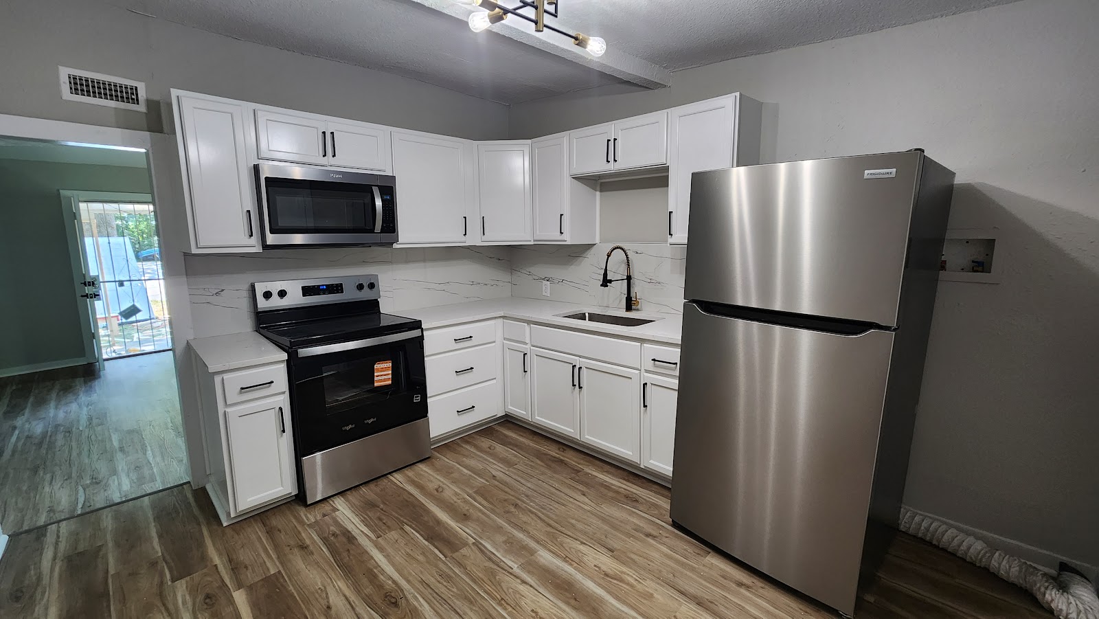 A bright finished kitchen with white cabinets, stainless appliances and wood floors.